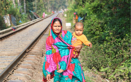 Amina Begum holdsa neighbour’s child as she stands on the railway line through Notun Bazar, a slum in Khulna, Bangladesh, September 10, 2021. Thomson Reuters Foundation/Mosabber Hossain